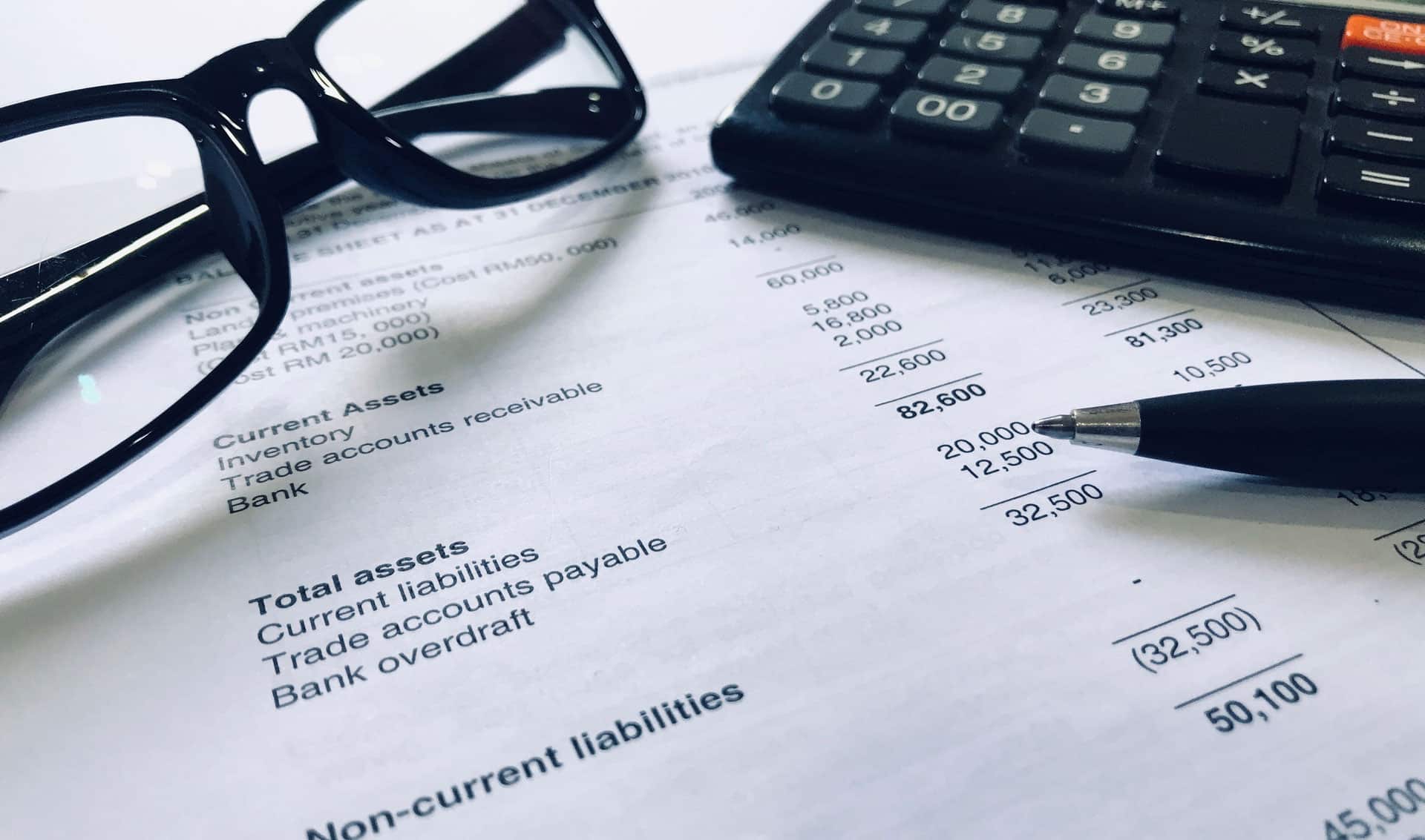 Papel com anotações, óculos, calculadora e caneta
