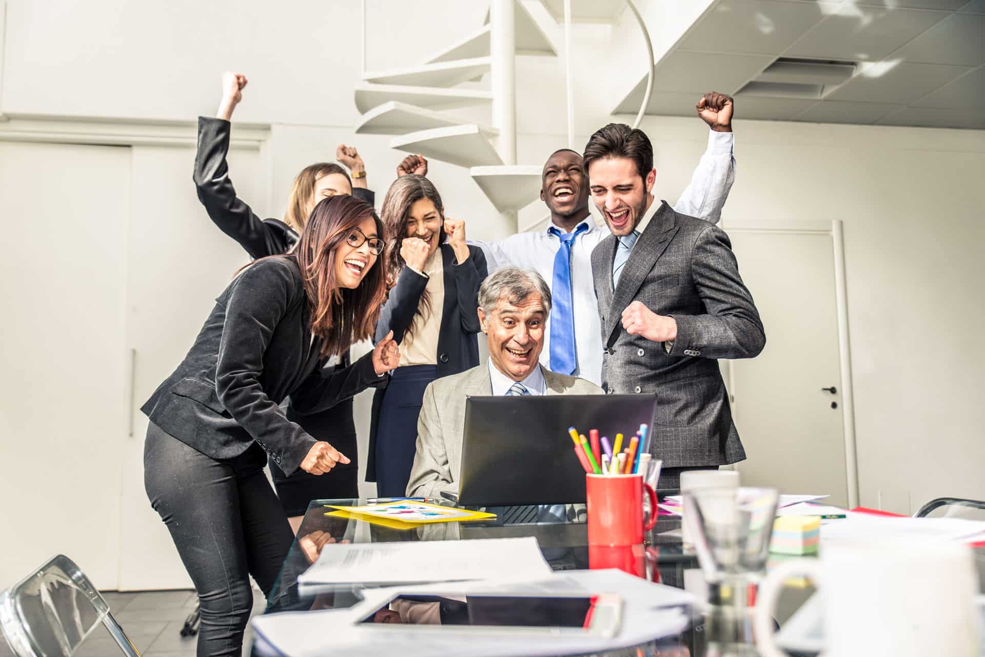 Pessoas reunidas em frente a um computador, comemorando. 