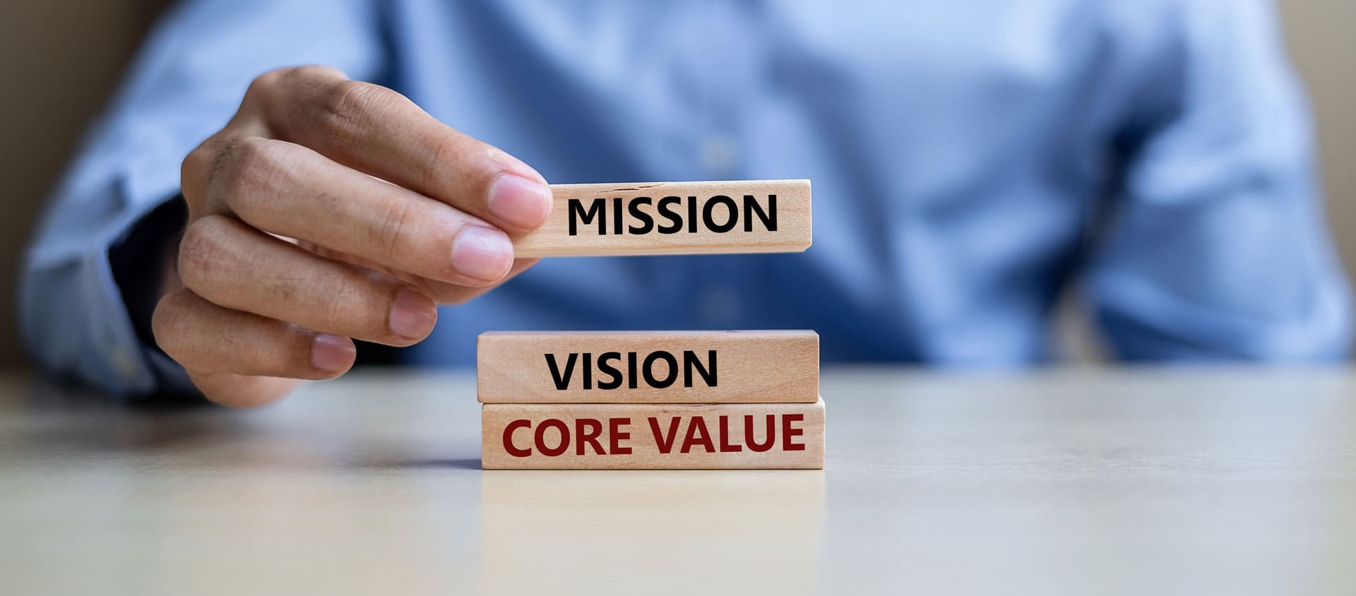 Homem empilhando 3 quadradinhos de madeira, cada um com as respectivas palavras: mission, vision, core value.