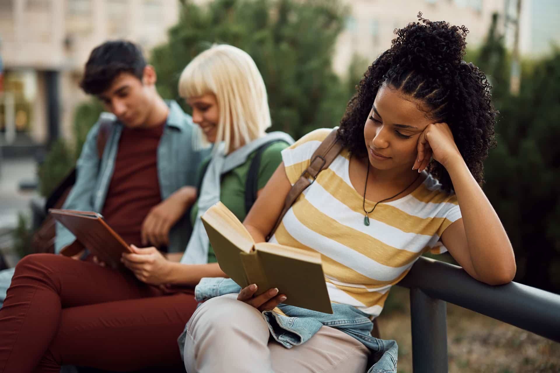 Pessoas sentadas em um banco lendo livros.