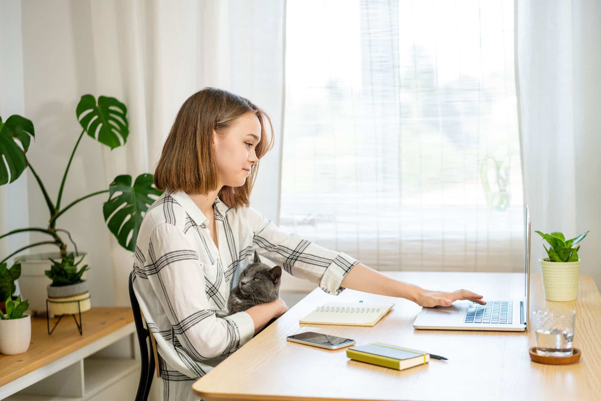 Jovem mulher trabalhando em home office com um gato no colo.